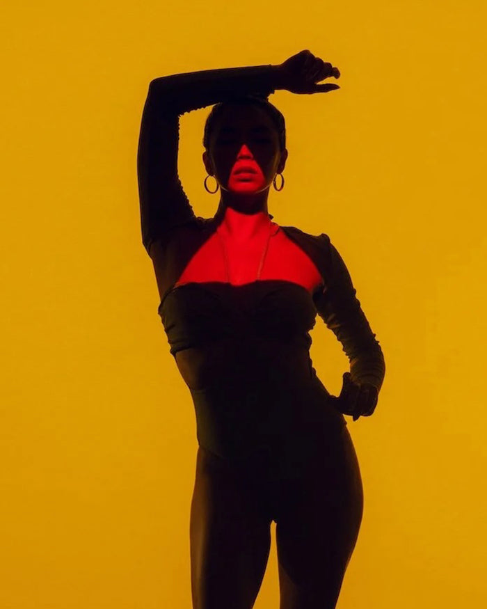 Women with arm on head posing in front of yellow wall. 